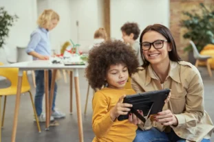 portrait of nice young female teacher smiling at camera while showing video on tablet pc to her